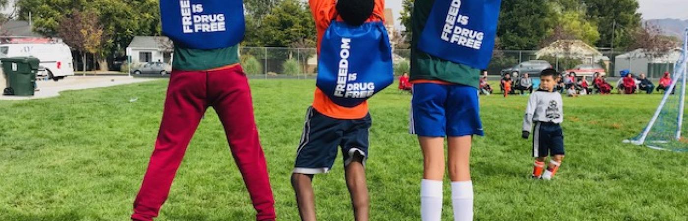 Kids with bags reading "Freedom is drug-free" jump on a field