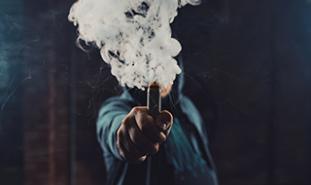 person holding vape pen with smoke coming out of it